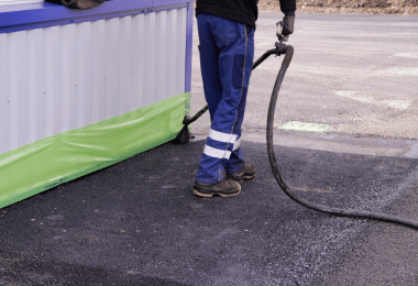 Photo d'une personne utilisant le Baticache vert sur une façade pour protéger contre les projections de goudron